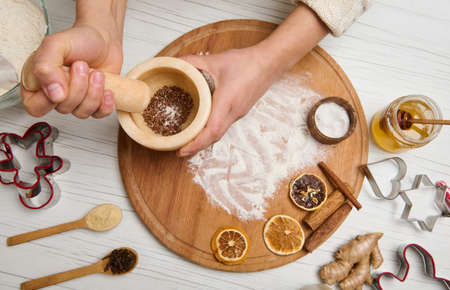 Woman's hands grinding ingredients in marble mortar, on a wooden board sprinkled with flour and...