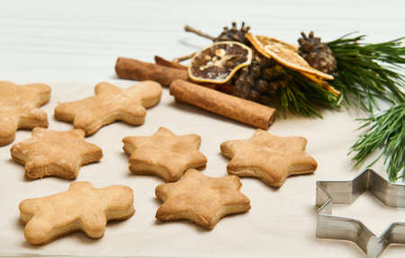 Gingerbread cookies as stars shape for Christmas, on a wooden surface with pine cones and branches,...