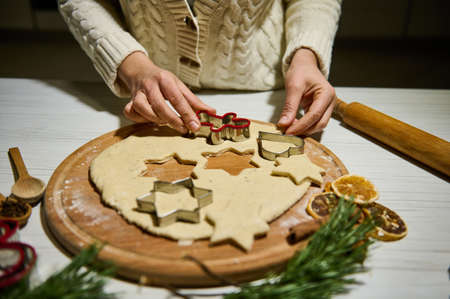 Woman cutting cookies of raw gingerbread dough. Christmas and New Year celebration traditions. Traditional festive food making, family culinary.の写真素材