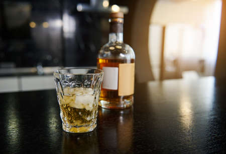 Soft focus on a faceted glass with a bottle of whiskey or other strong alcoholic drink on a bar countertop at kitchen homeの写真素材