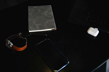 High angle view of office accessories, laptop, earphones on the box, watch, mobile phone and gray notepad on wooden deskの写真素材