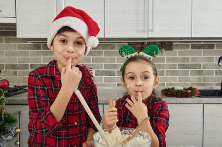Cheerful adorable children in checkered red and green clothes looking at the camera holding a finger...