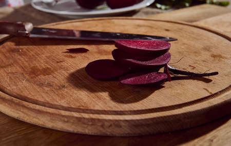 Food background. Close-up of burgundy raw beet slices on a cutting wooden board and a kitchen knife.