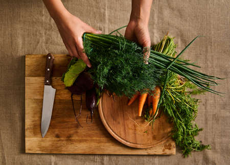 Overhead view of hands holding a bunch with fresh wet green dill above a wooden cutting board with...