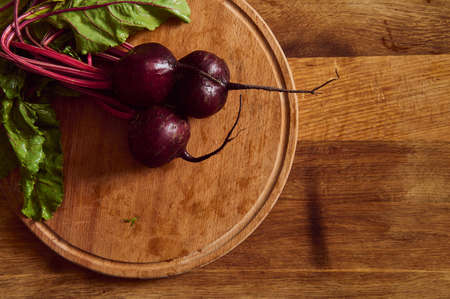 Flat lay. Overhead view of a bunch of fresh burgundy beetroot with green tops and leaves on a wooden...