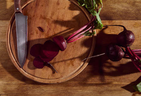 Overhead view of sliced burgundy fresh raw seasonal beet with tops on a wooden board with a kitchen knife. Flat lay food backgroundの写真素材
