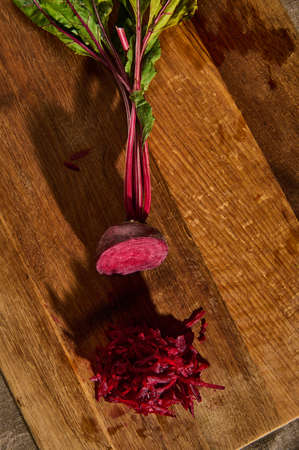 Top view of fresh juicy raw burgundy beetle with tops, half shredded on a grater on a wooden kitchen...