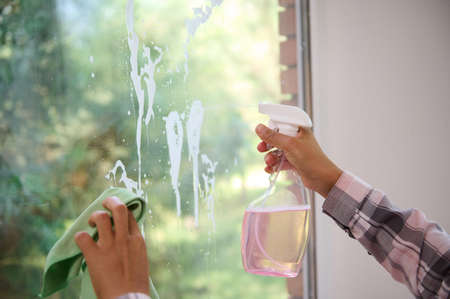 Close-up of the hands of an unrecognizable woman cleansing the window, removing stains by spraying...