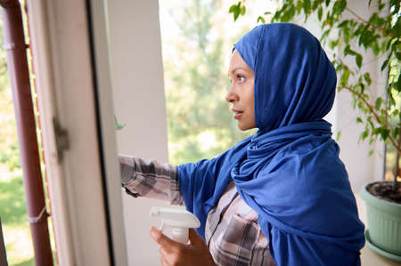 Close-up of confident beautiful young Arab Muslim woman with covered head in blue hijab washing...