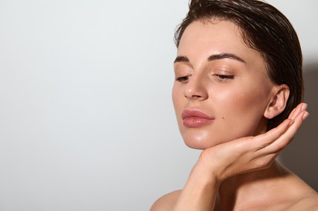 Close up face portrait of dark haired elegant European woman with healthy clear glowing skin touching her face. Cosmetology, skin care concept with copy ad spaceの写真素材