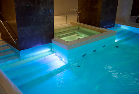 View of a beautiful spacious interior with an indoor thermal pool with beautiful underwater lighting in a luxurious lounge area of a health spa resortの写真素材