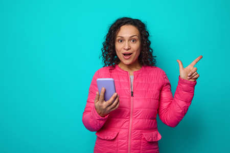 Happy curly haired brunette, beautiful African woman in pink jacket, with wide open eyes in surprise...