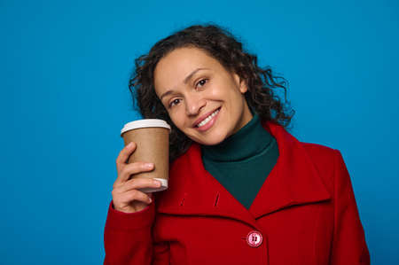 Portrait of a charming dark-haired pretty woman in green pullover and bright red coat holds...