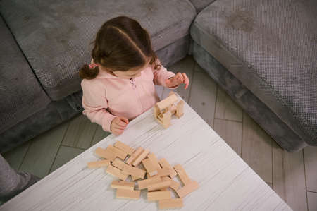 Overhead view of creative preschool child, concentrated baby girl on building with wooden blocks...