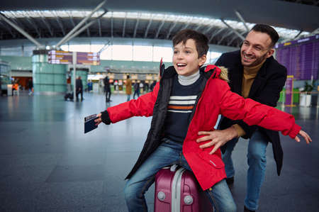 Charming little boy with a passport and a boarding pass in his outstretched hands while his dad is...