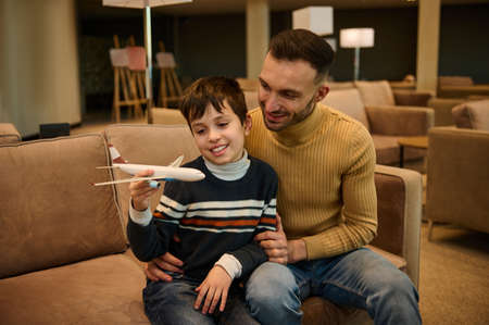 Adorable little boy plays with a toy plane while his loving father sits next to him, hugs him,...