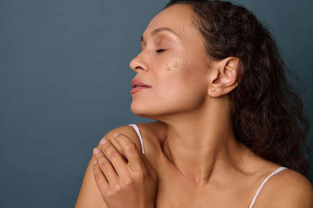 Charming dark-skinned beautiful woman with closed eyes posing on a gray background with dots of...