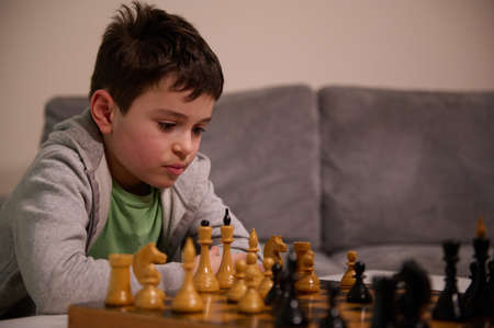Concentrated Caucasian school aged boy developing chess strategy, playing board game with friend. Logic development, leisure board games, entertainment, intelligent hobby and education conceptの写真素材