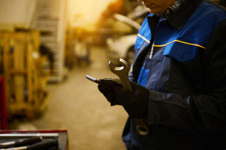 Close-up of the hand of a technician, mechanic in professional uniform with wrench at repair shop. Automobile warranty repair and maintenance conceptの写真素材