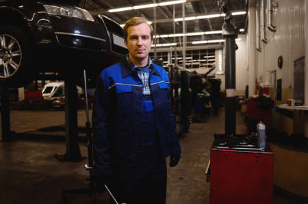 A technician, auto mechanic, car engineer standing against the background of a lifted automobile...