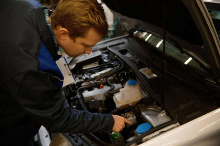 Overhead view of a young professional auto mechanic inspecting the car under hood, examining the...