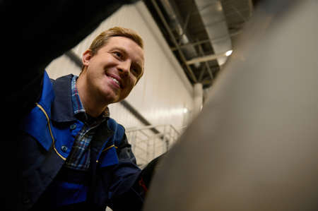 Close-up portrait of a garage mechanic, car engineer, technician working in repair shop, inspecting car engine during regular warranty vehicle maintenanceの写真素材
