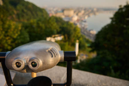 Tourist telescope looks at city with view of Kiev and the Dnieper River. Close-up old metal binocular standing on a hill with a beautiful view of the old historic city. Panoramic observation of natureの写真素材