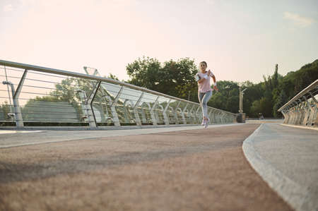 Full length portrait of determined sportswoman running on a treadmill along a city bridge,...