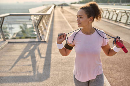 Beautiful mixed race woman in sportswear standing on a treadmill on the city bridge with a jumping...
