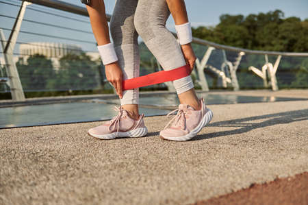 Close-up. Crop of the legs of an unrecognizable female athlete exercising with resistance fitness band, doing body weight training outdoor on the city bridge. Weight loss, fitness and sport conceptの写真素材