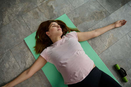 Sporty woman in anticipation of a baby lying on a yoga mat and doing relaxing and stretching...