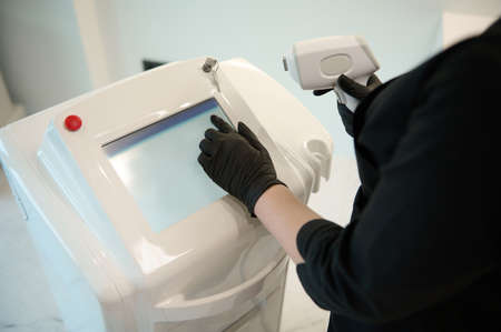 Apparatus for laser hair removal and the hands of a doctor-cosmetologist in medical black gloves,...