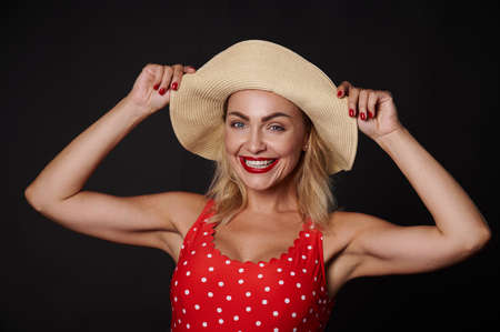 Attractive Caucasian blonde pretty woman in a straw summer hat and red swimsuit with white polka...