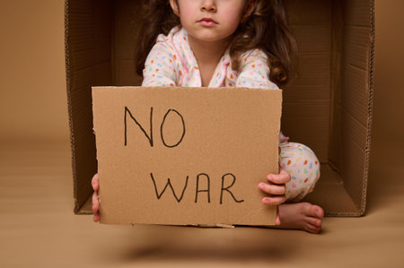 No War written in a cardboard poster in the hands of European child little girl refugee or migrant during political and military conflicts in the country, isolated over beige background, copy ad spaceの写真素材