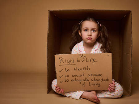 Adorable little Caucasian girl holding a cardboard poster with social message, calling for respect her rights, isolated over beige background with copy space. World Children's Day on July 1st.の写真素材
