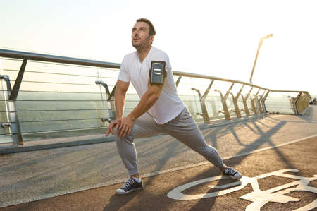 Young jogger sportsman preparing for the training. Athlete performing lunges, stretching his legs...