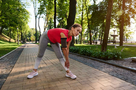Athletic girl in sport tight clothes doing stretching after the early morning jog. Middle aged...