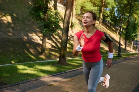 Female runner, charming middle aged sportswoman in tight sportswear enjoying morning jog in the city park on a beautiful summer dayの写真素材