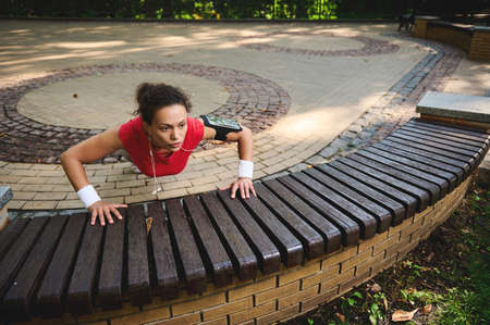 Determined active beautiful woman exercising outdoors,pushing ups from wooden bench while performing full body functional cross training outdoors. Sport, body weight training, weight loss conceptの写真素材
