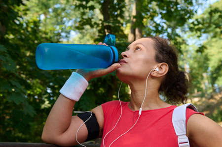 Close-up of an exhausted beautiful sportswoman drinking water from bottle, refreshing and hydrating...