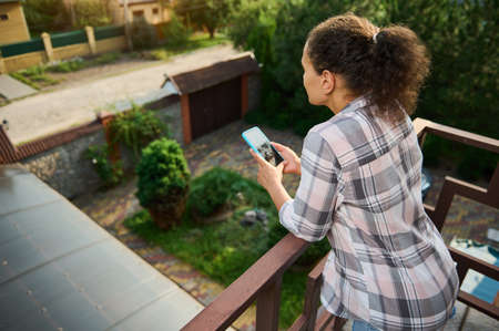 View from the back to a young dark-haired woman in casual clothes using mobile phone, browsing,...