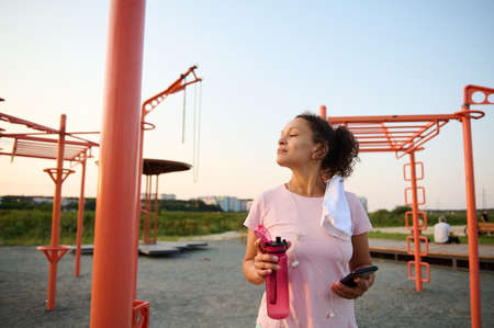 Sportswoman, African American fit girl, athlete in pink t-shirt standing on a sports field with a...