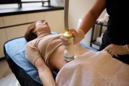 Beautiful young woman on a daybed receiving hardware spa procedure for cellulite reduction and weight loss in medical clinic.の写真素材