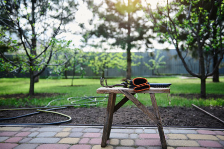 Garden tool and work gloves on an old wooden stool against the background of a backyard garden