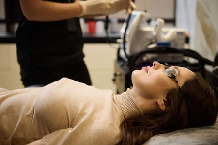 Side portrait of a beautiful Caucasian woman wearing protective UV goggles before getting laser skin...