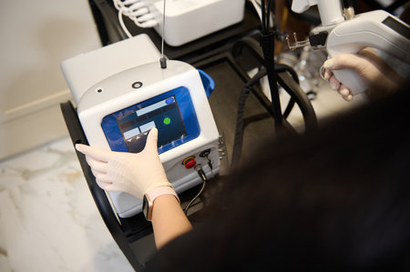 Overhead view of the hands of aesthetician in a black uniform holding a laser resurfacing machine...