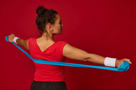 Close-up of young beautiful Hispanic fit sportswoman working out with elastic rubber strap against...