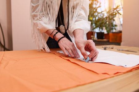 Detail of tailor's hands using soap transfers a sewing pattern on an orange colored satin fabric in his fashion design studio. Tailoring atelier, clothing designer, creative profession conceptの写真素材