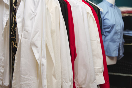 Details of women's clothes hanging on hangers in clothing design and tailoring atelier of fashion boutique. Cropped image of exclusive women's shirt on hangersの写真素材