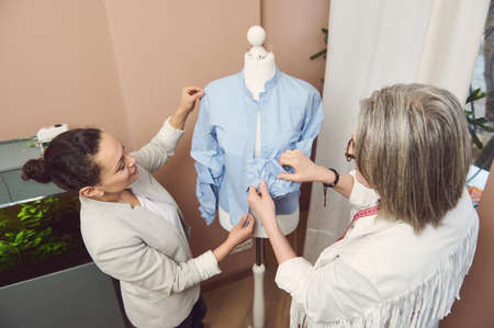 View from above to a team of multi-ethnic and diverse female fashion designers tailors trying on a handmade classical shirt from new collection on mannequin in a fashion design and tailoring atelierの写真素材